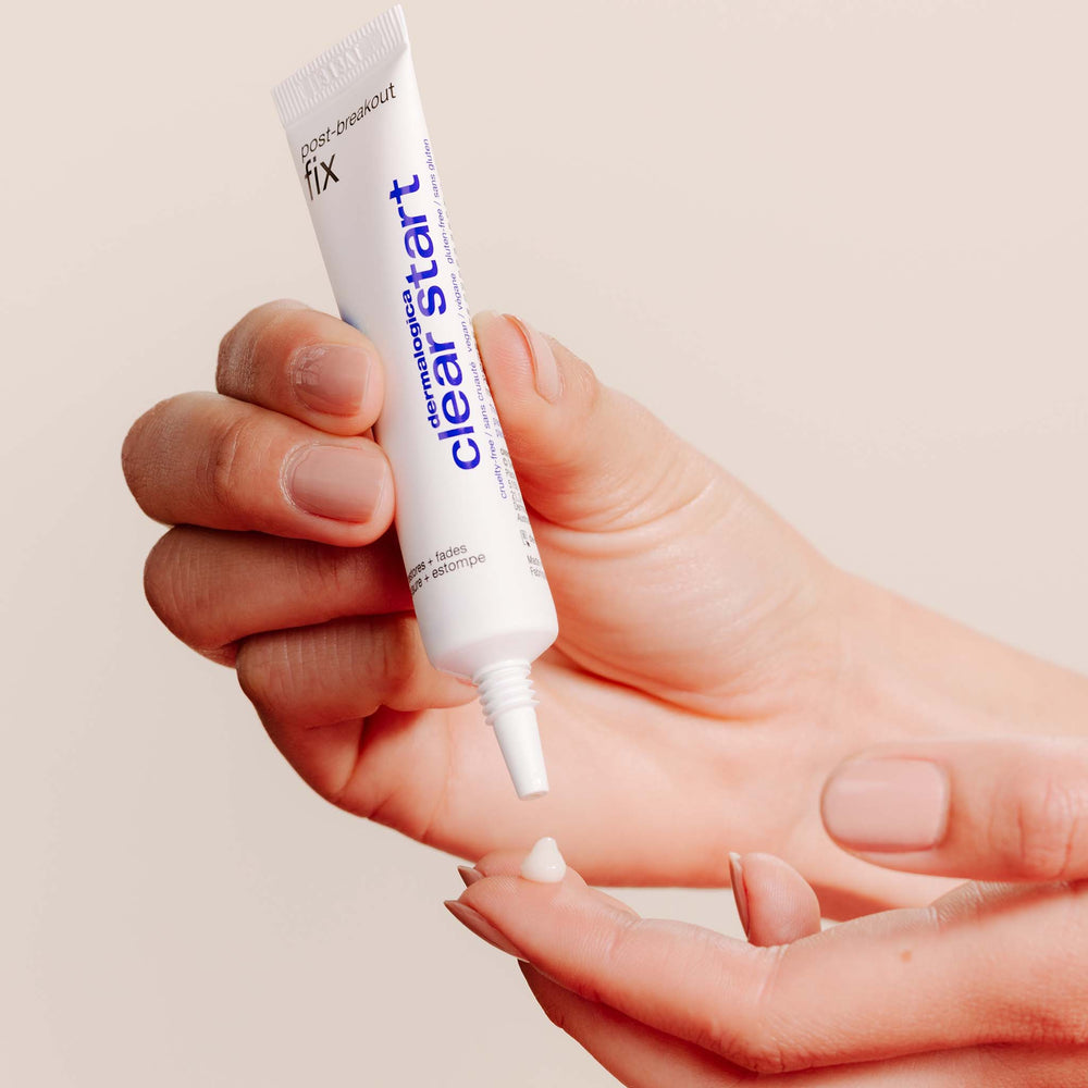 Hand holding a tube of 'Clear Start' skin care product against a beige background