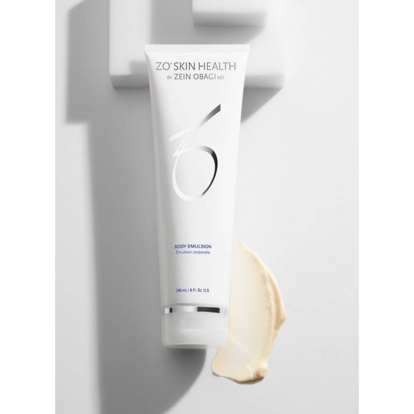 ZO Skin Health by Zein Obagi Body Emulsion 240mL in a white squeeze tube, shown against a white background with a smear of the light beige lotion at the base. The Facial Maestro