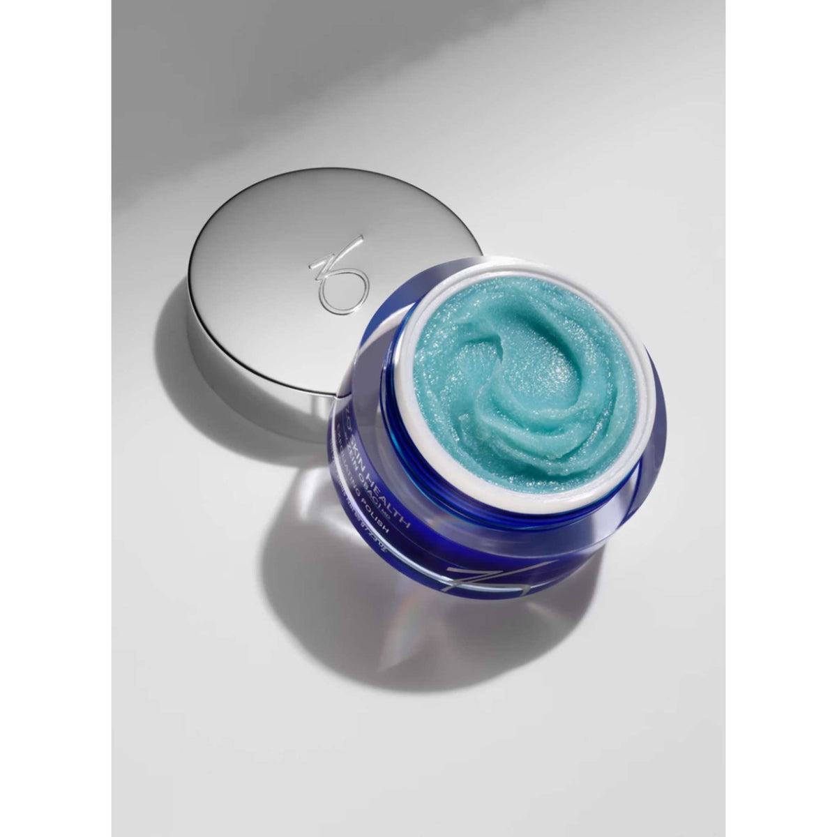 An open jar of blue cream Exfoliating Polish with a metallic silver lid, showing a swirled light blue-green cream inside, photographed on a clean light gray background.