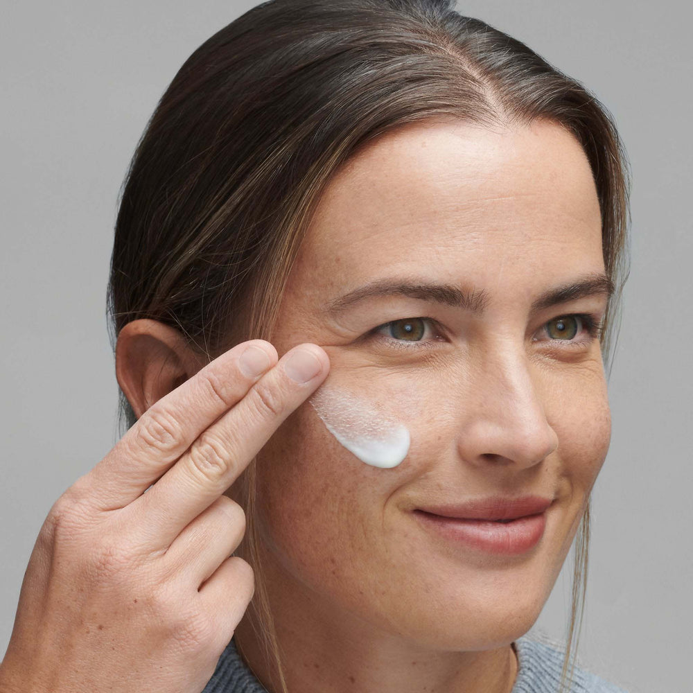 Woman applying powerbright moisturizer to her face against a gray background